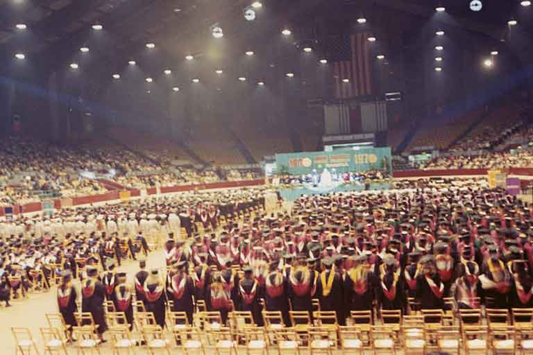 A stadium packed with IUPUI's first graduates in caps and gowns. Color photo.