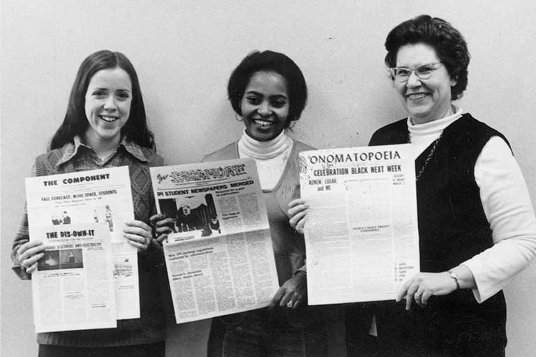 Two students and an advisor hold previous campus newspapers, The Component and Onomatopoeia, as well as the new Sagamore student publication. Black and white photo.